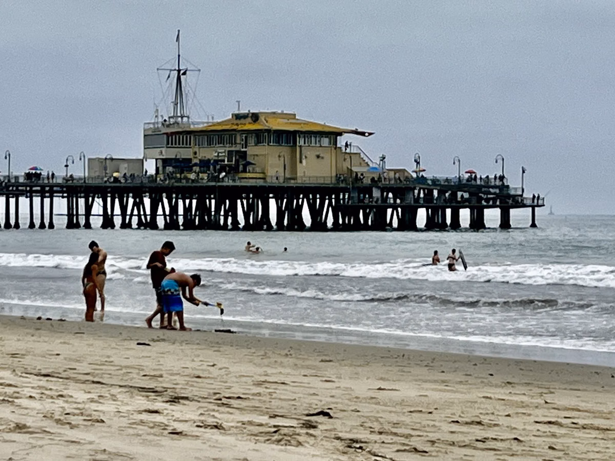 The end of the Santa Monica Pier seen from the beach, with people in the shallows